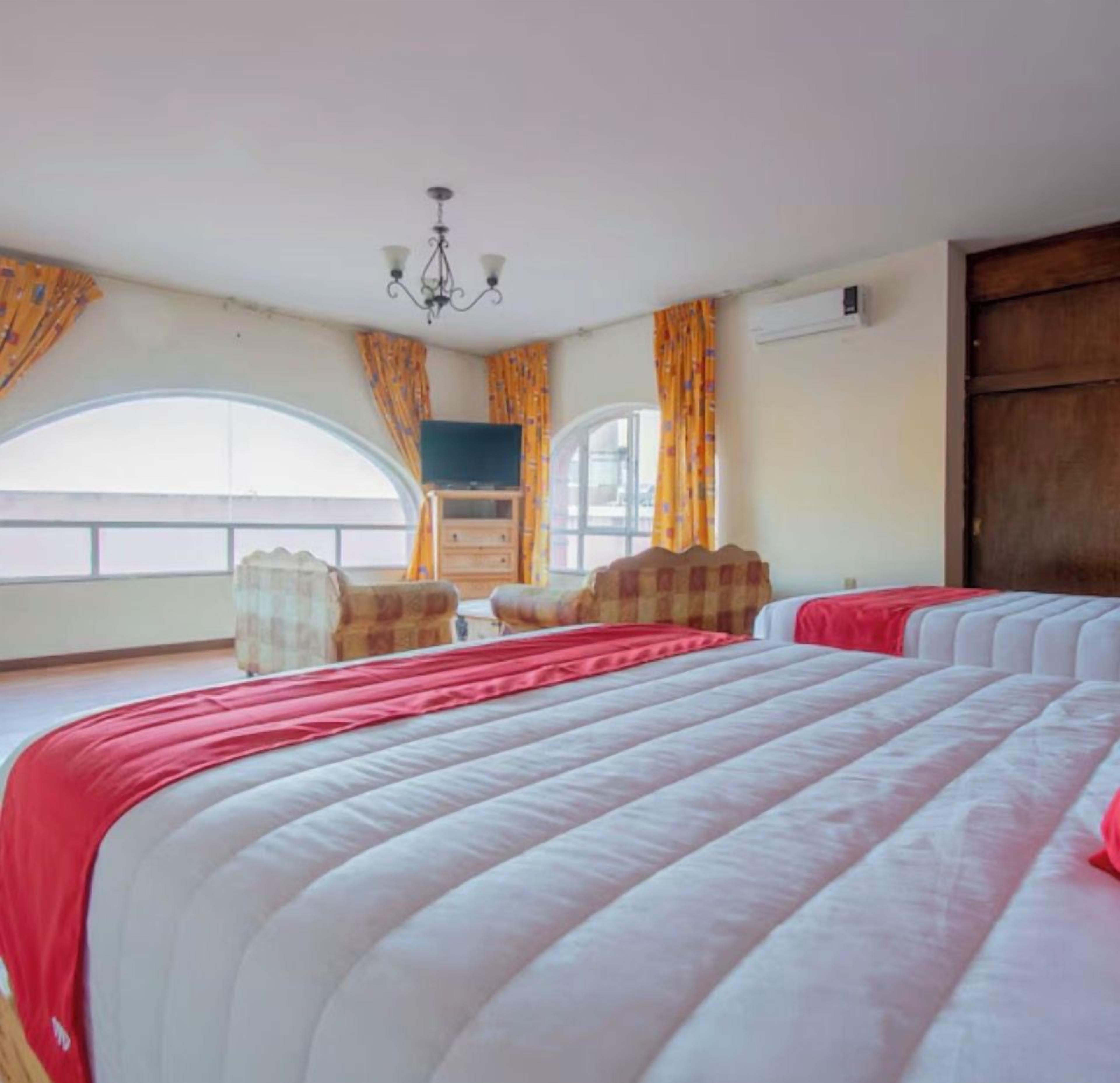A hotel room with a large bed, a television, a wooden dresser, and a window with curtains.