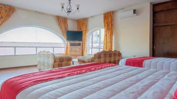 A hotel room with a large bed, a television, a wooden dresser, and a window with curtains.