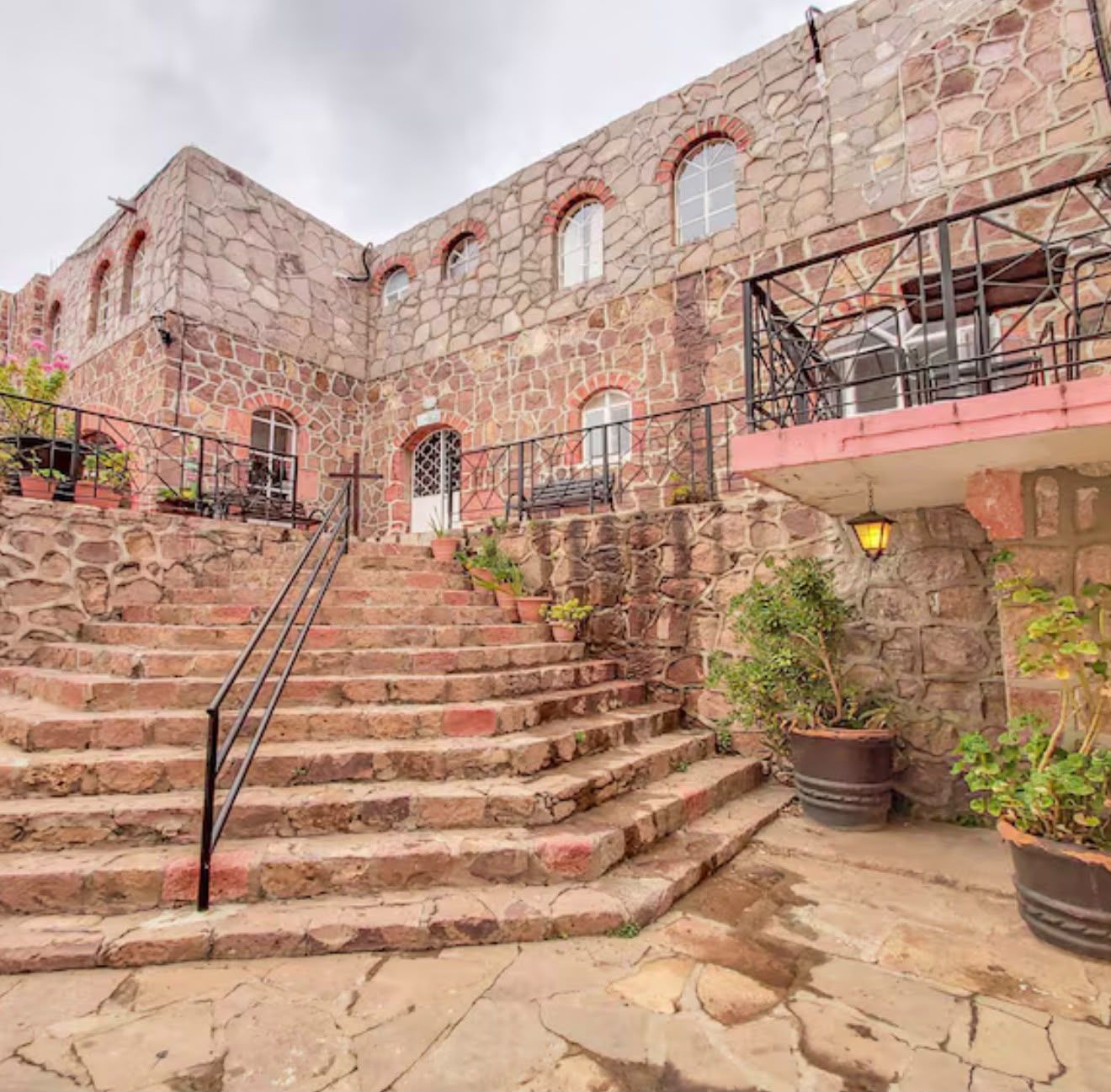 Un edificio de piedra con una escalera que lleva a un balcón con mesas al aire libre.