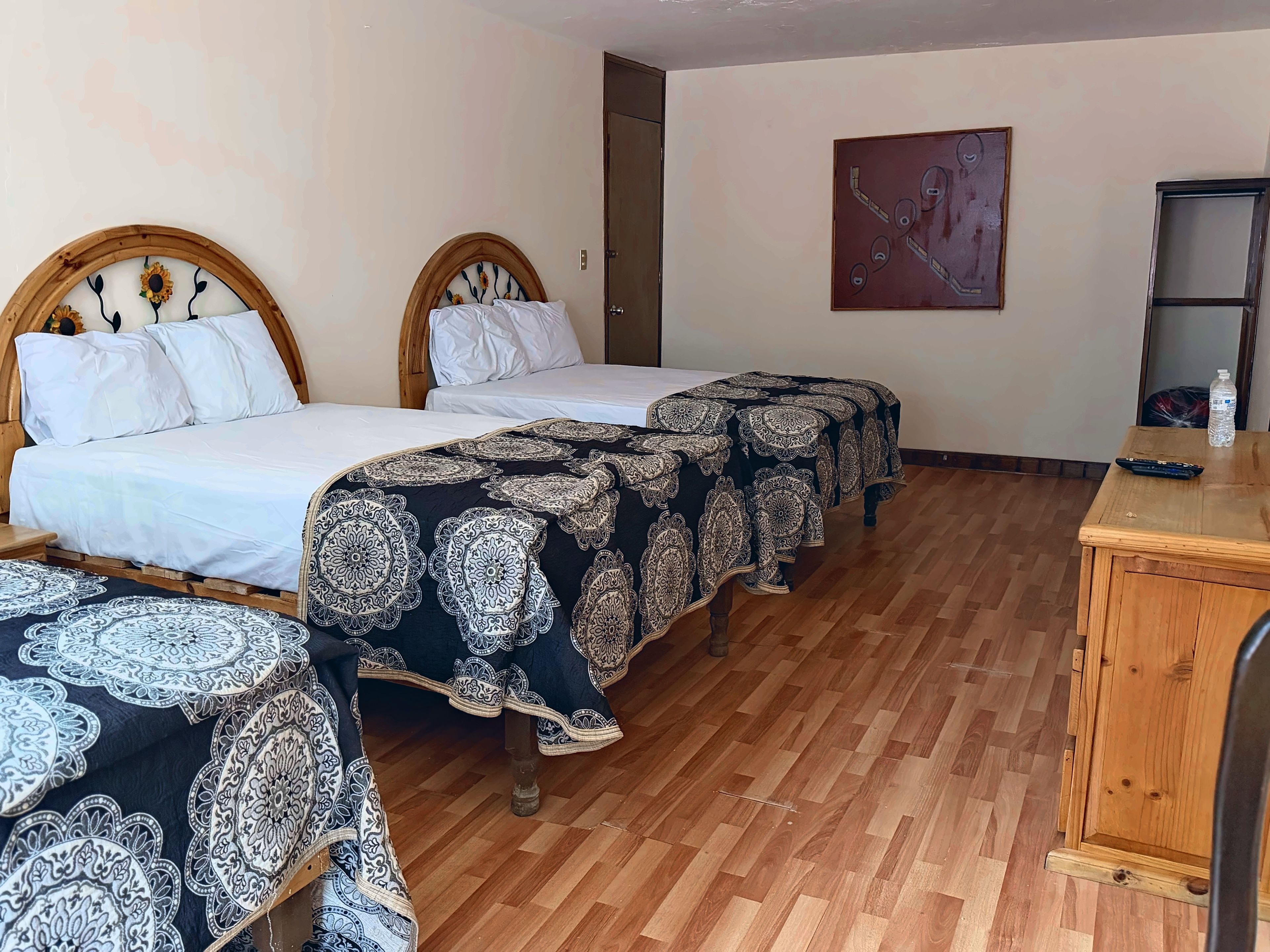 Habitación de hotel con dos camas, suelo de madera, una mesa con un control remoto y una botella de agua.