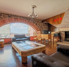 A cozy living room with a stone arch, a fireplace, and a large window overlooking a cityscape. - Hotel casa del gobernador Zacatecas (zacatecas)