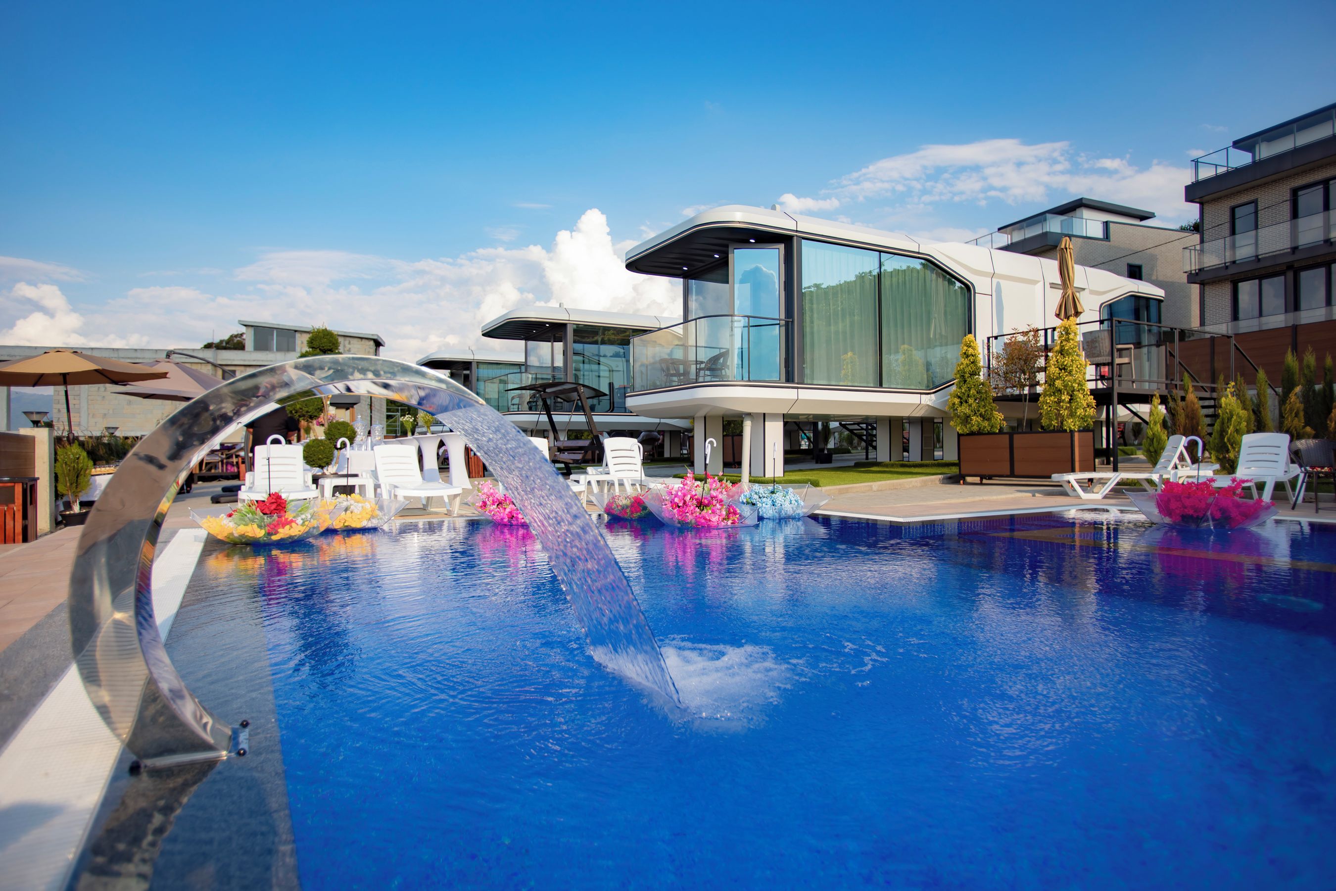 Un hotel moderno con piscina, sillas de descanso y fachada de vidrio.