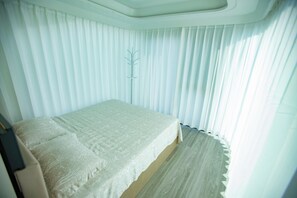 A room with a bed, a coat rack, and a window with curtains.