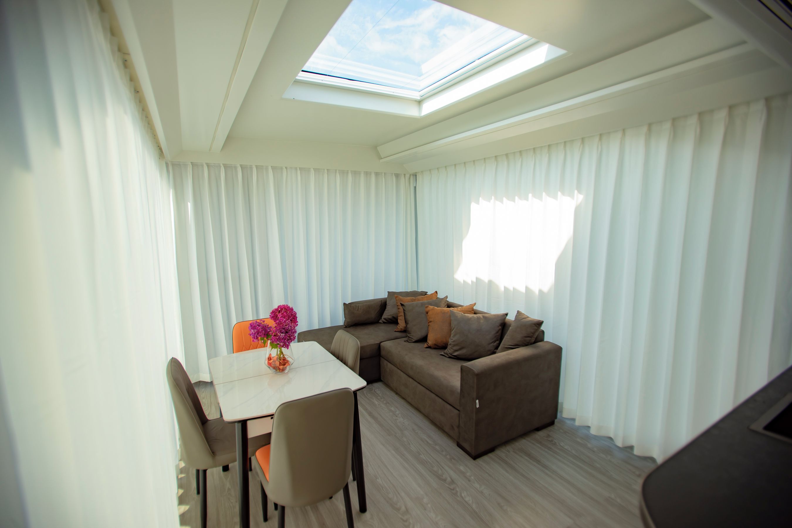 A modern living room with a sofa, a dining table, and a skylight.