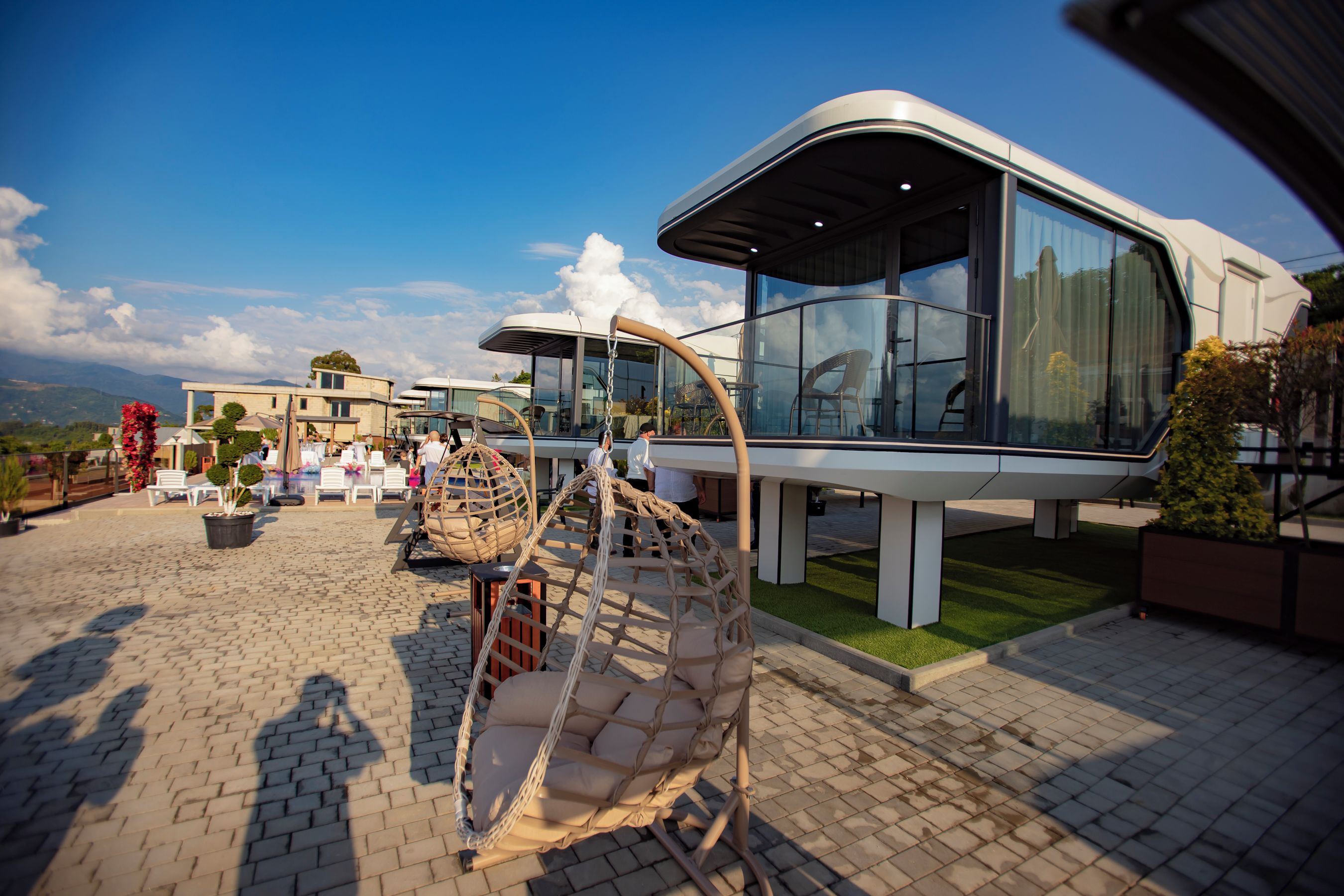 A modern outdoor seating area with a swing chair, a glass-enclosed structure, and a paved patio.