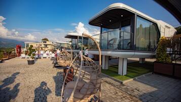A modern outdoor seating area with a swing chair, a glass-enclosed structure, and a paved patio.