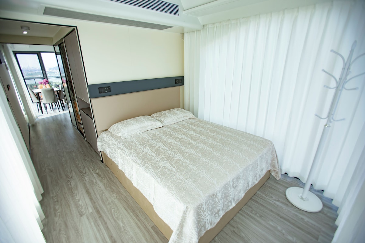 Quarto de hotel com cama, mesa de cabeceira, janela com cortinas e vista para a cidade.