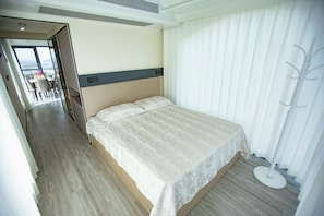 Habitación de hotel con cama, mesita de noche, ventana con cortinas y vistas a la ciudad.