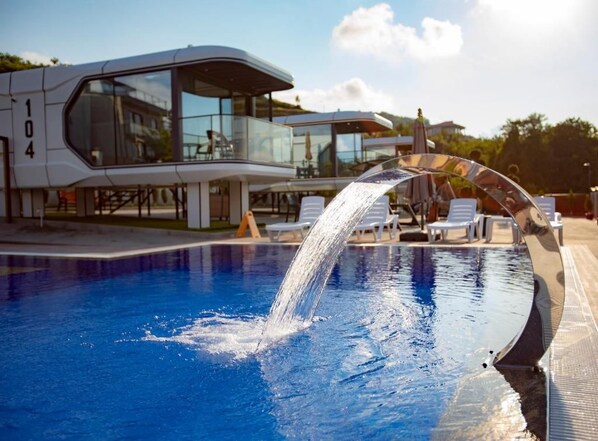 A swimming pool with a water feature, lounge chairs, and a modern building with glass windows.
