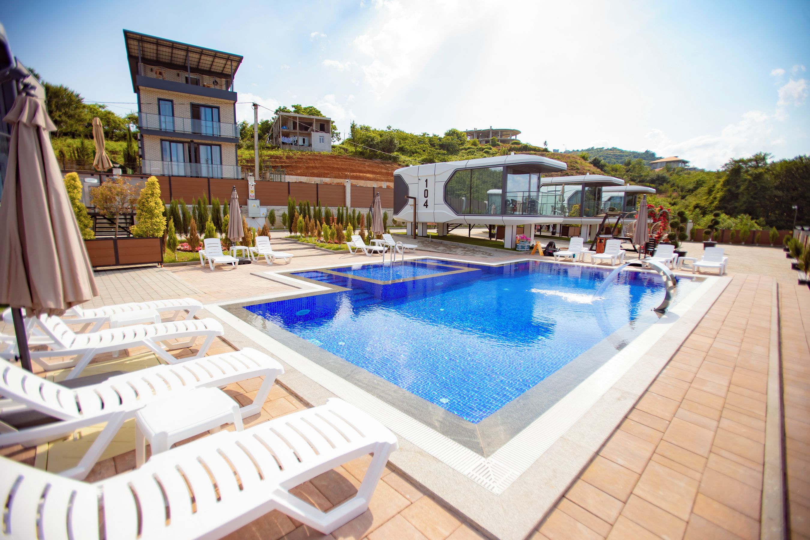 A swimming pool with lounge chairs, a modern building, and a landscaped area with trees.