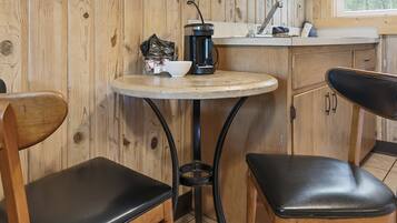 A small kitchen area with a round table, two black chairs, a coffee maker, and a window with a view of trees.