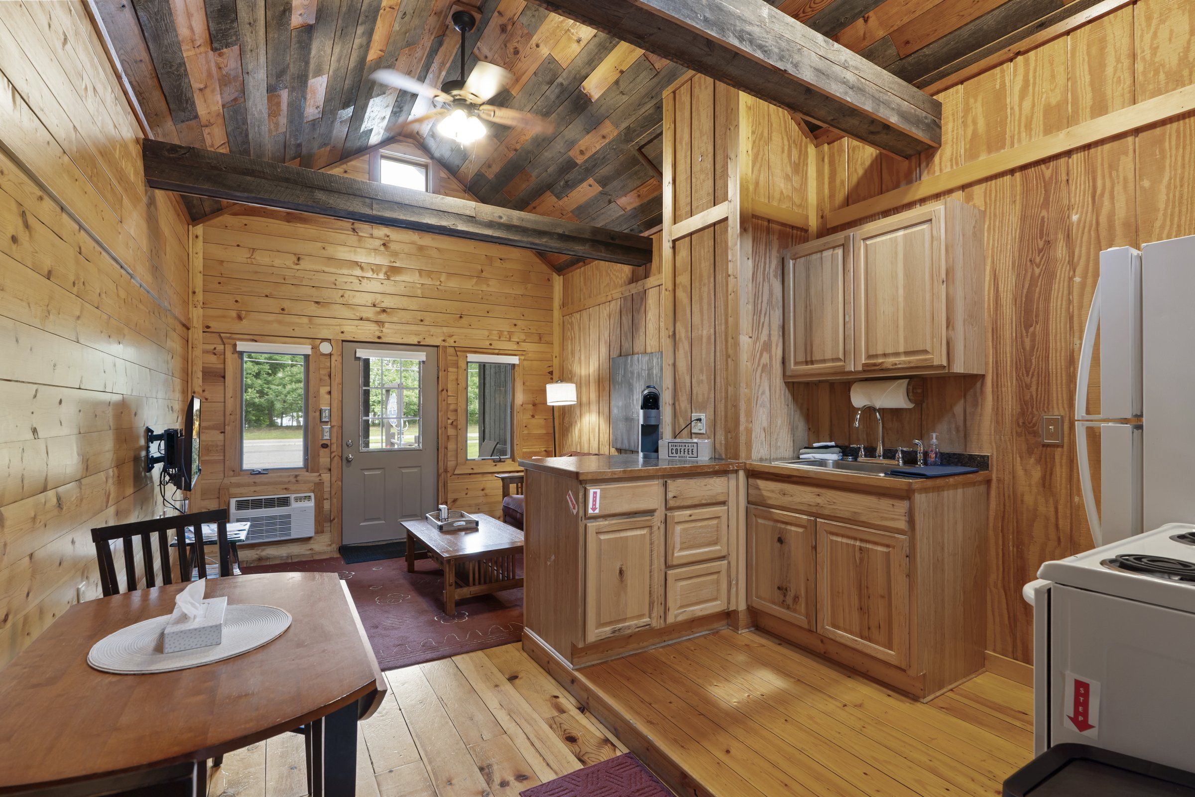 Interno di una baita in legno con zona pranzo, angolo cottura e ventilatore a soffitto.