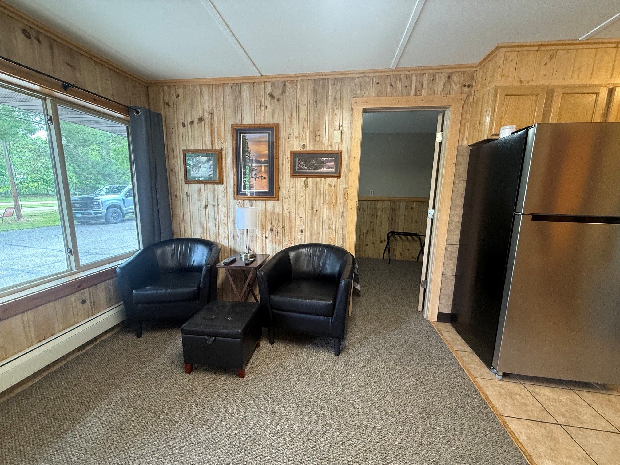 A room with two leather chairs, a small table, a refrigerator, and wooden paneled walls.