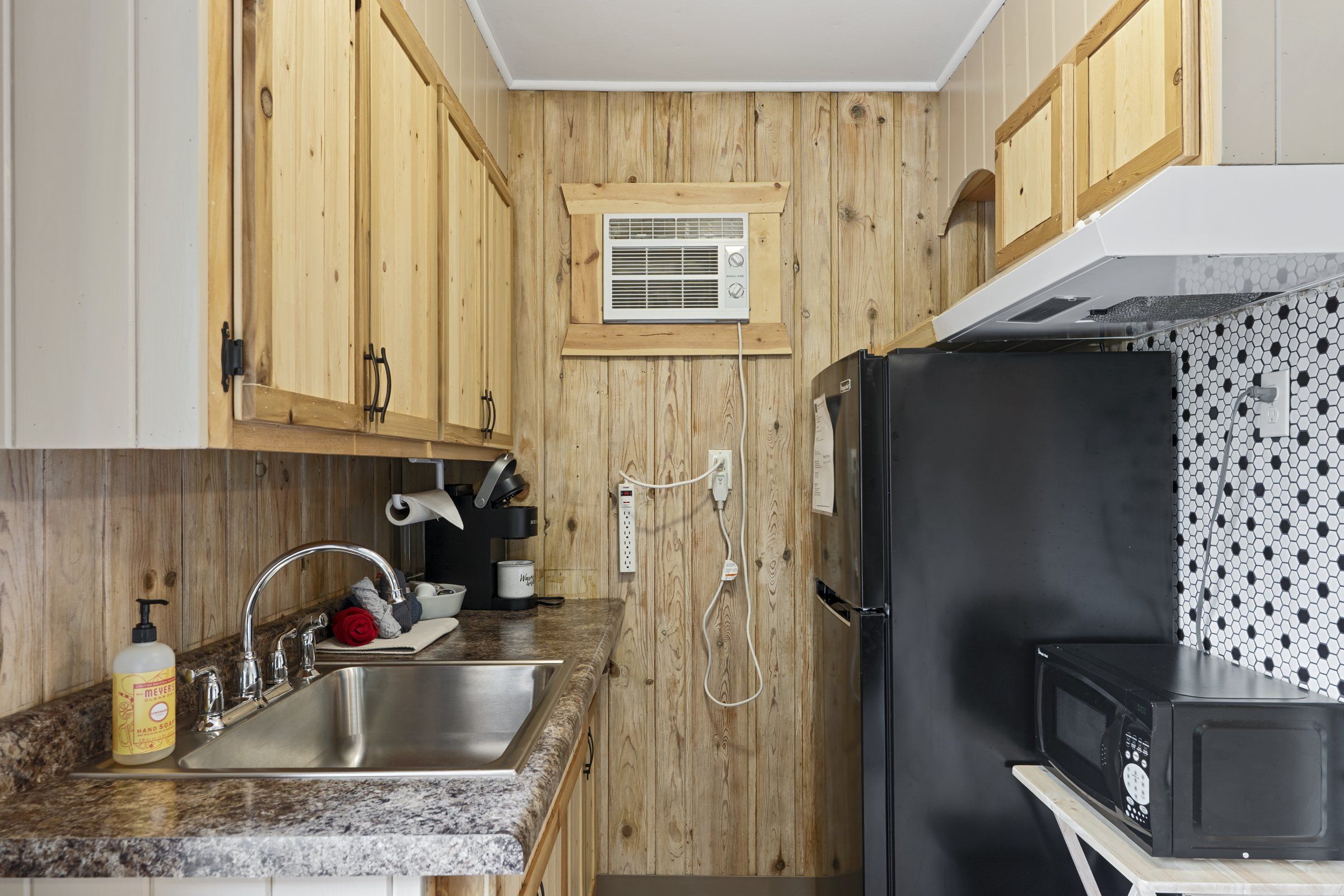 A kitchen with wooden cabinets, a stainless steel sink, a black refrigerator, and a microwave.