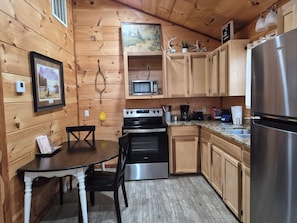 Eine Küchenzeile im Chalet-Stil mit Esstisch, Stühlen, Herd, Mikrowelle und Kühlschrank.