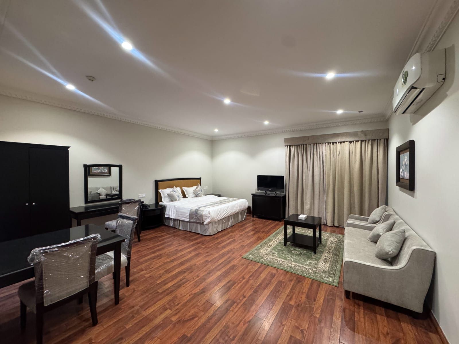 A hotel room with a bed, a desk, a chair, a sofa, and a television.