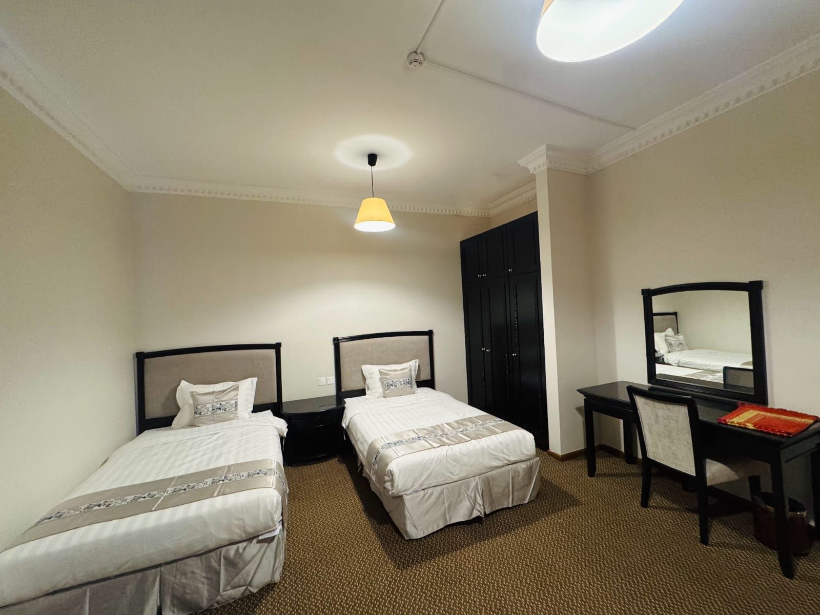 A hotel room with two single beds, a desk with a chair, a wardrobe, and a mirror.