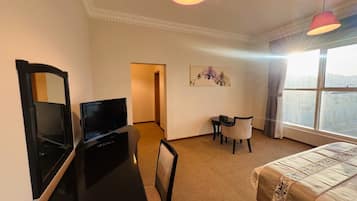A hotel room with a bed, a desk with a television, a chair, a small table, and a painting on the wall.