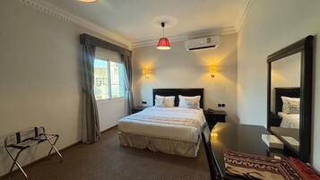 A hotel room with a bed, bedside tables, a desk, a chair, a mirror, and a window with curtains.