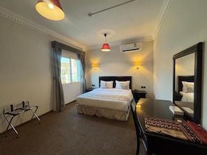 Habitación de hotel con cama, mesitas de noche, escritorio, silla, espejo y ventana con cortinas.