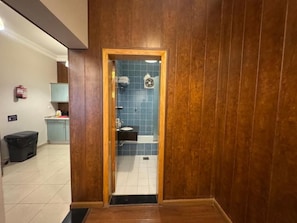 A wooden-paneled bathroom with a blue-tiled shower area, a visible sink, and a door leading to a hallway. - Al Jawhara Suite Serviced Apartments 2 (Taif)