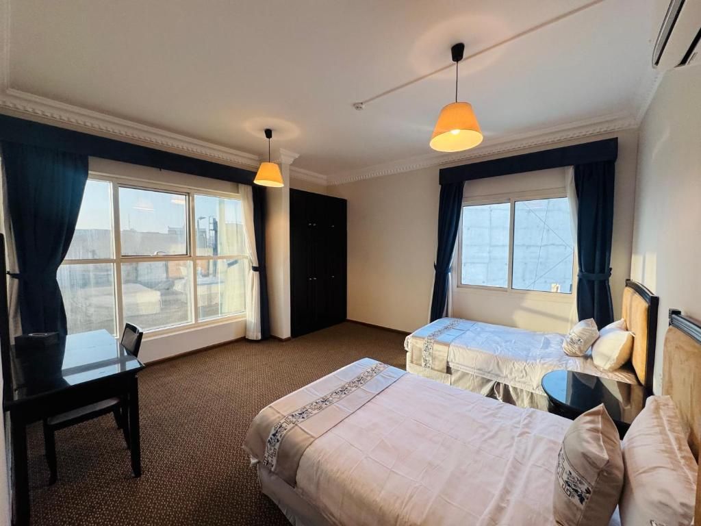 A hotel room with two beds, a desk, and a window.