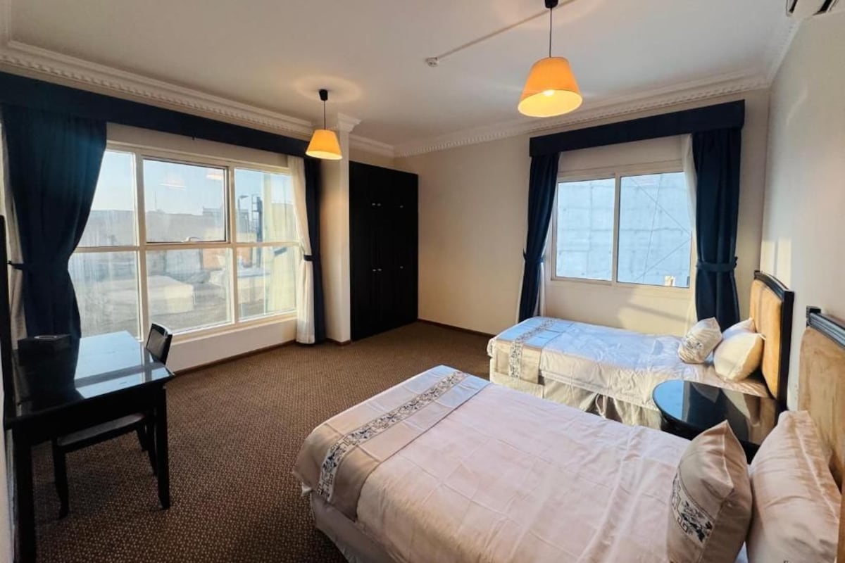 A hotel room with two beds, a desk, and a window.