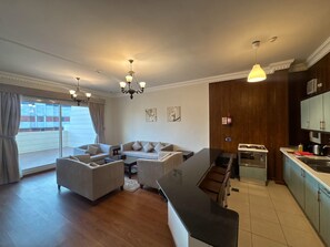A modern living room with a sofa set, a dining area with a kitchen in the background, and a large sliding glass door leading to an outdoor balcony.