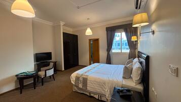 Une chambre d’hôtel avec un lit, un bureau, une télévision et une fenêtre avec des rideaux.