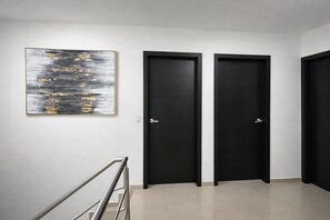 A hallway with two black doors, a staircase with a metal railing, and a large abstract painting on the wall.