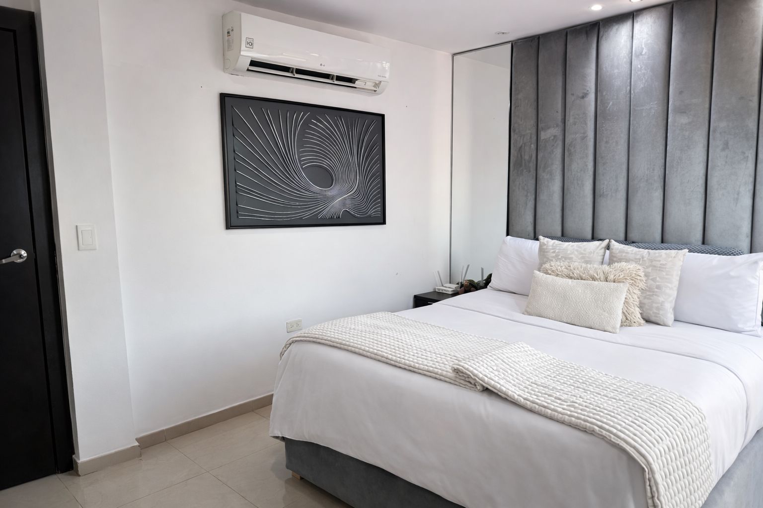 A modern bedroom with a bed, a wall-mounted air conditioner, a framed abstract artwork, and a grey headboard.
