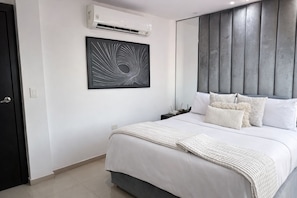 A modern bedroom with a bed, a wall-mounted air conditioner, a framed abstract artwork, and a grey headboard.