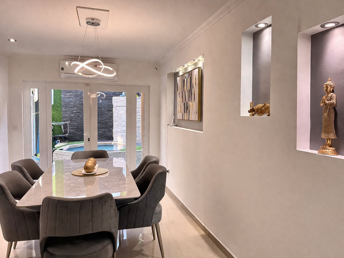 A modern dining area with a glass table and chairs, a ceiling light fixture, and a wall-mounted artwork.
