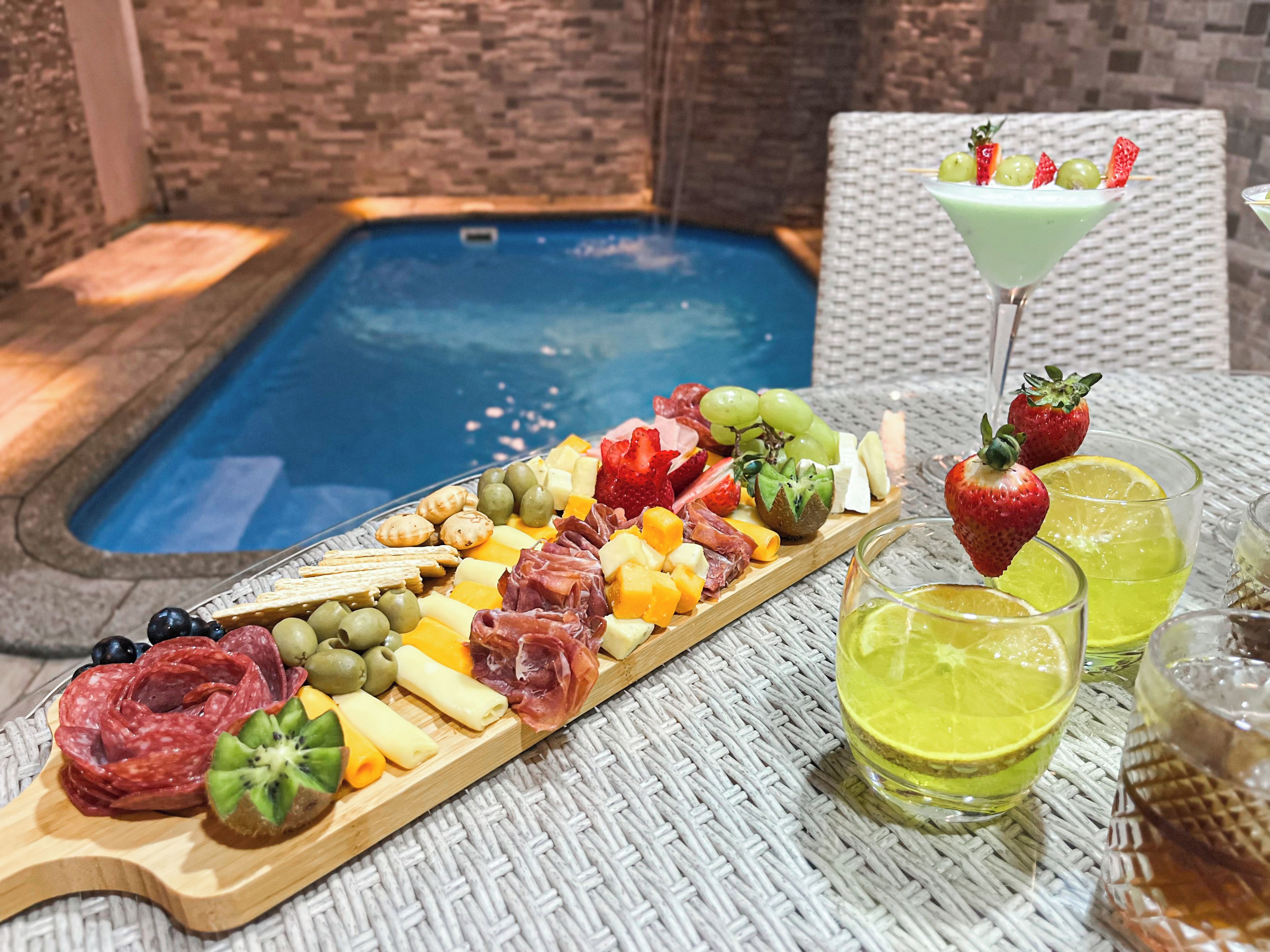 Escena junto a la piscina con una tabla de fiambres, una copa de martini y bebidas.