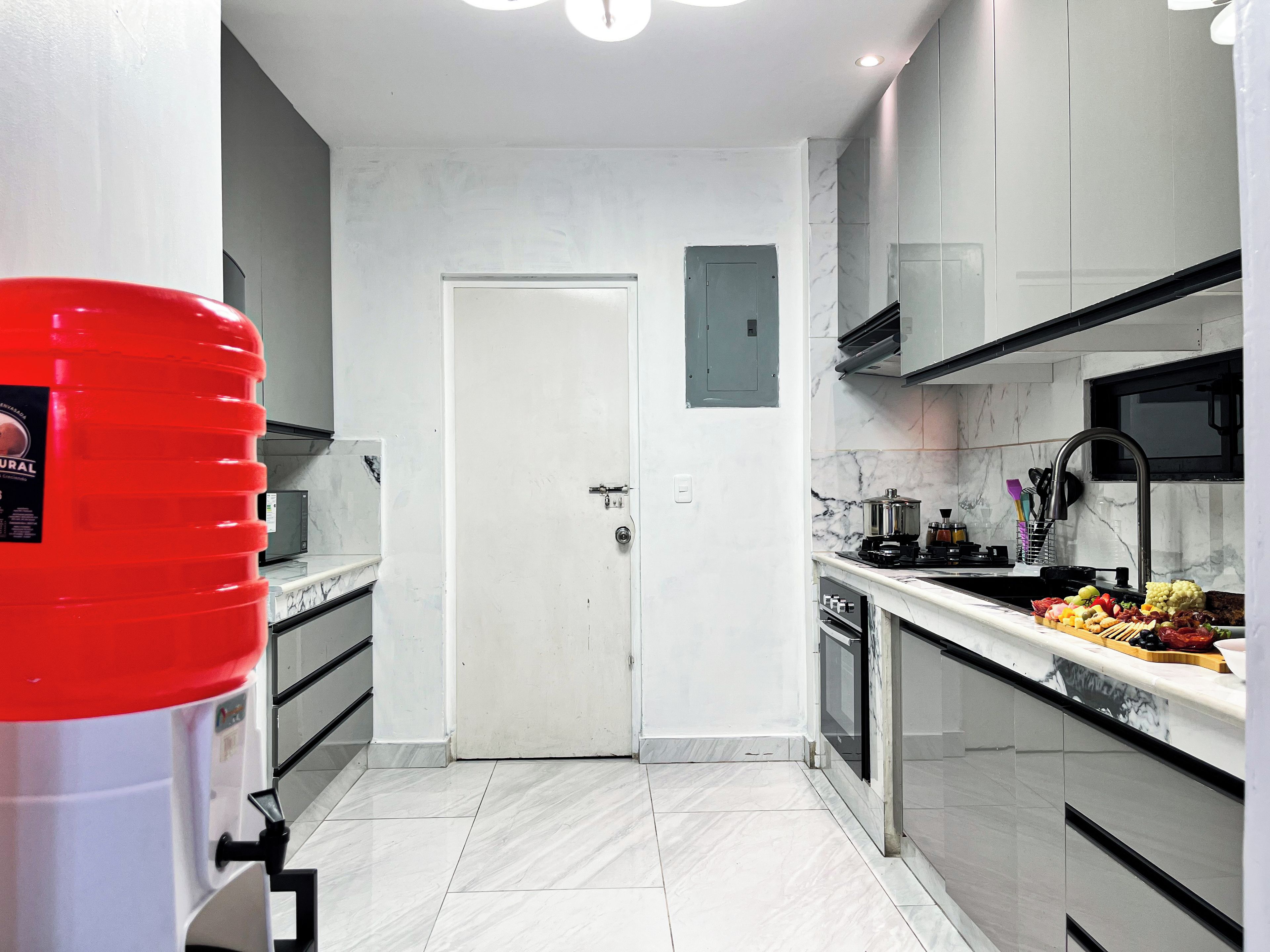 Una cucina moderna con mobili bianchi, un piano di lavoro in marmo e un erogatore d'acqua rosso.