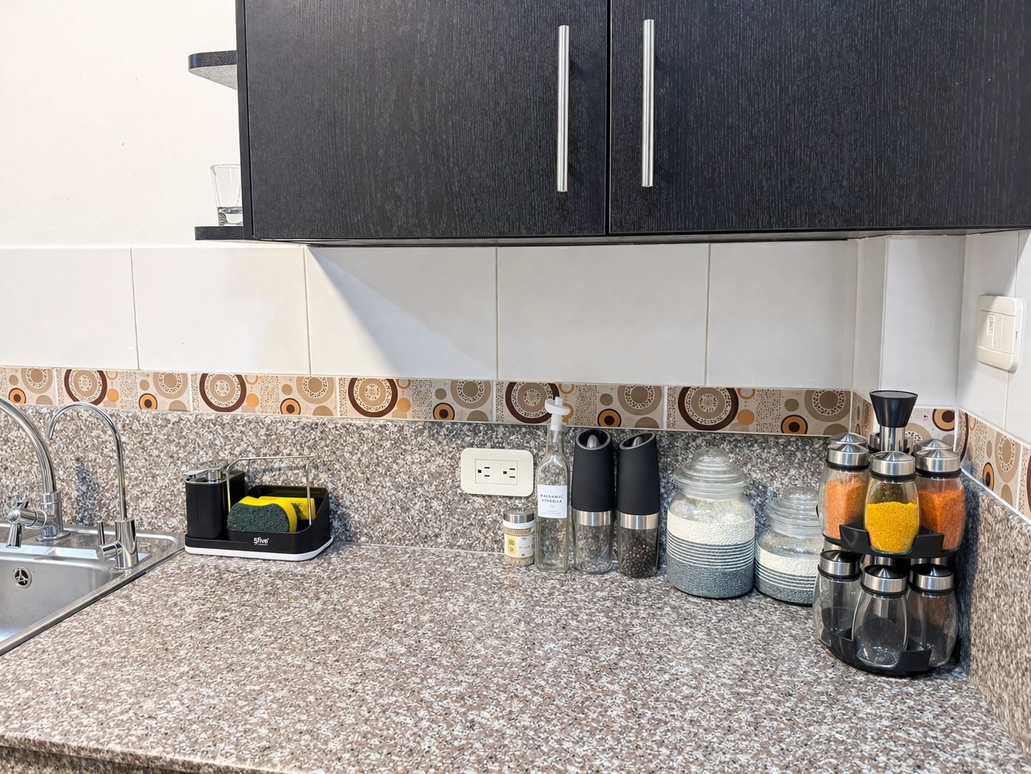 A kitchen with a granite countertop, a black cabinet above, and a patterned backsplash.
