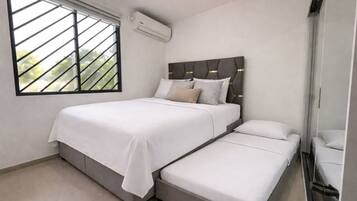 A bedroom with a bed, a smaller bed, a window with blinds, and an air conditioning unit.