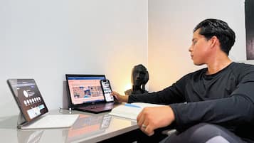 Una persona sentada en un escritorio con una computadora portátil, una tableta y un teléfono inteligente.