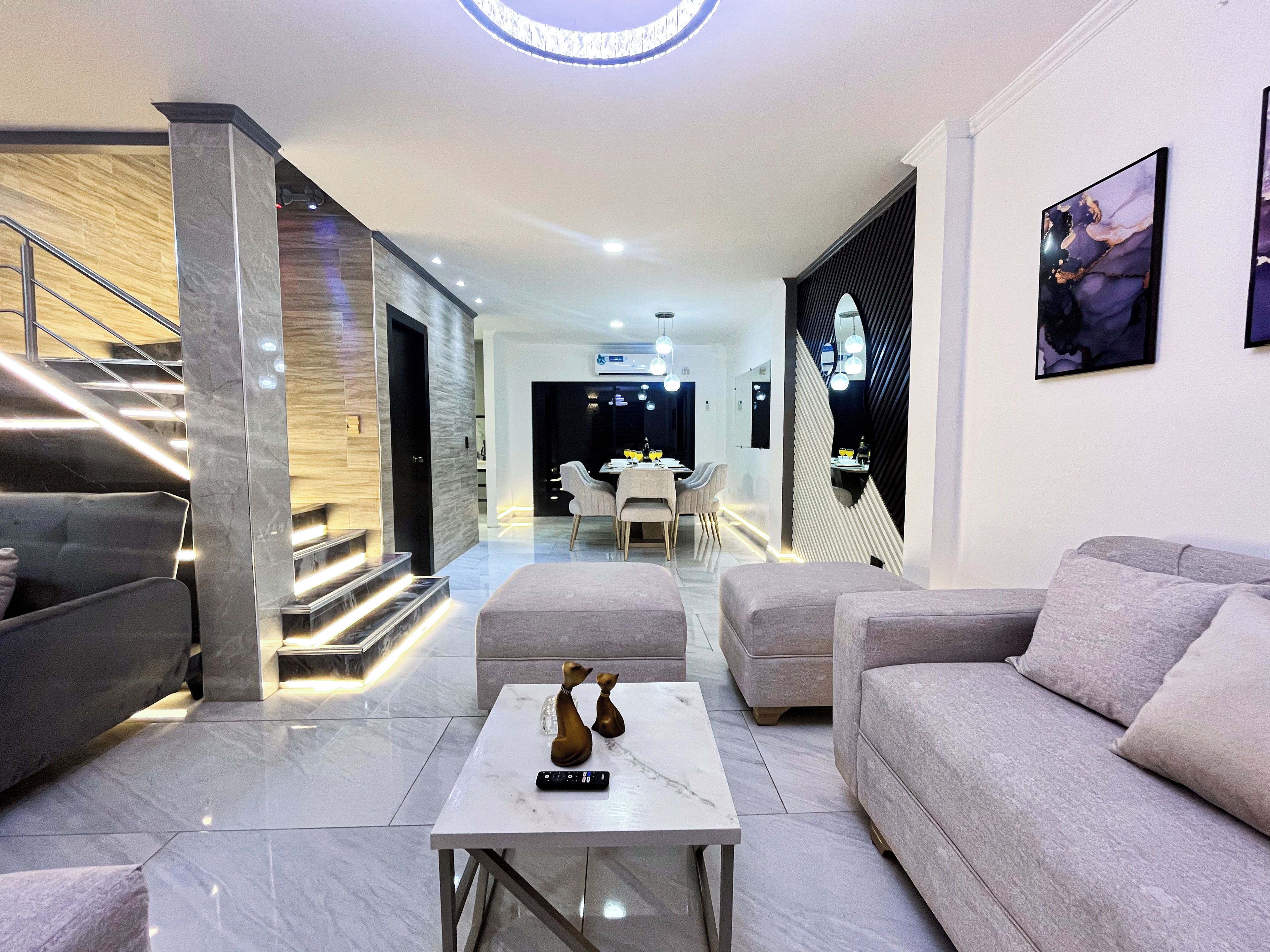 A modern living room with a marble coffee table, grey sofas, and a staircase leading to an upper level.