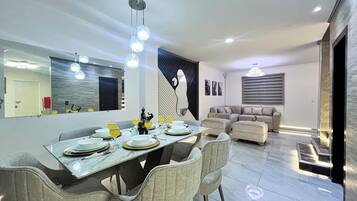 Zona pranzo moderna con tavolo in marmo, sedie rivestite in grigio e lampadario.