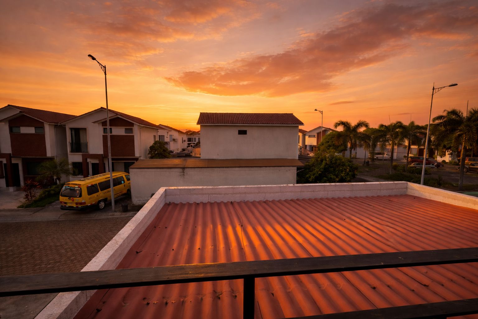 A residential area with a flat-roofed building, a yellow van, and a sunset sky.