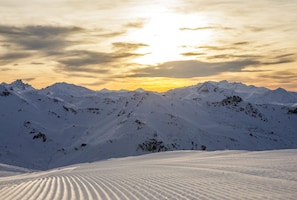 Eine verschneite Berglandschaft mit klarem Himmel und untergehender oder aufgehender Sonne.