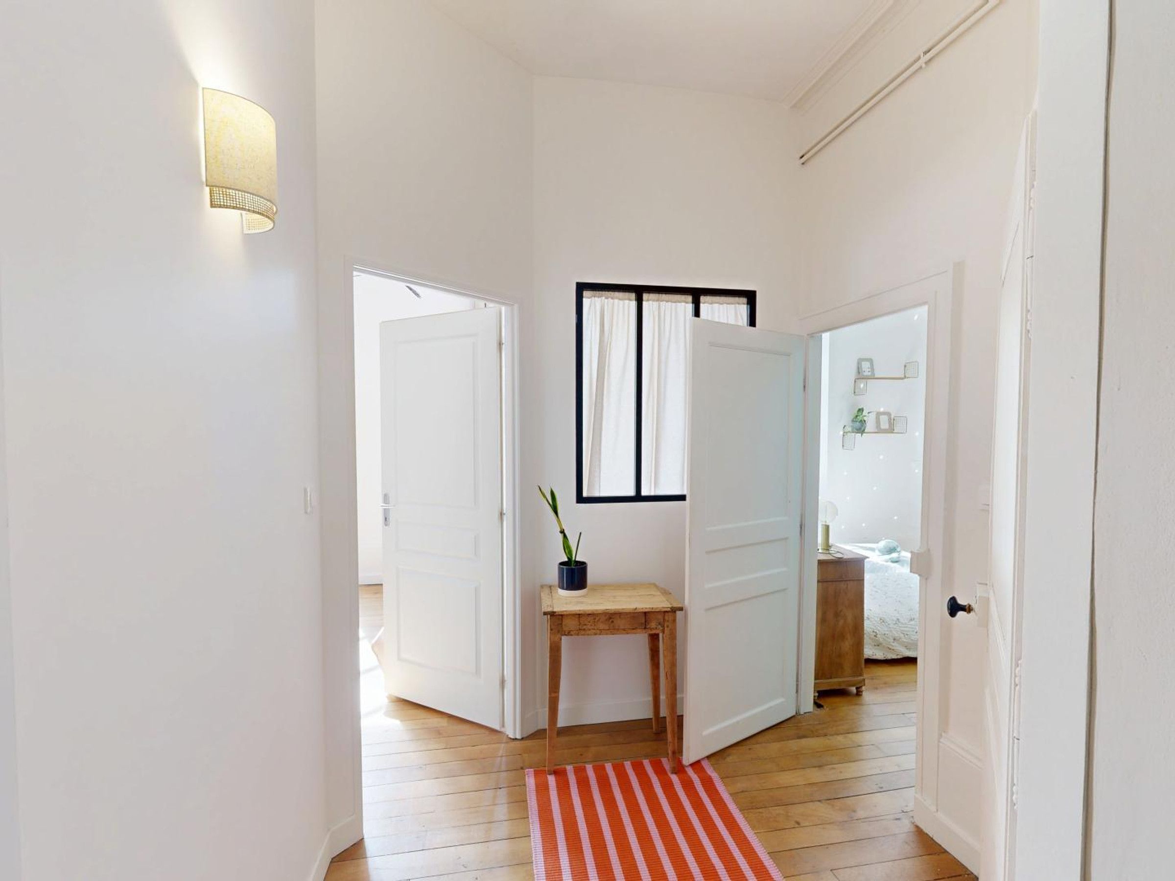 A hallway with wooden flooring, white doors, a small table with a plant, and a red and white striped rug.