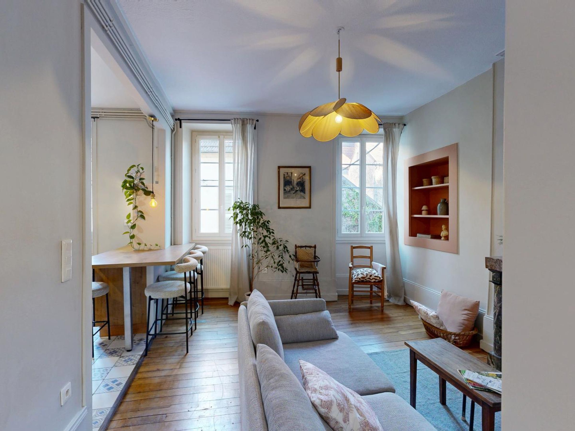 Ein modernes Wohnzimmer mit einer Couch, einem Essbereich mit Barhocker und einer hängenden Leuchte.