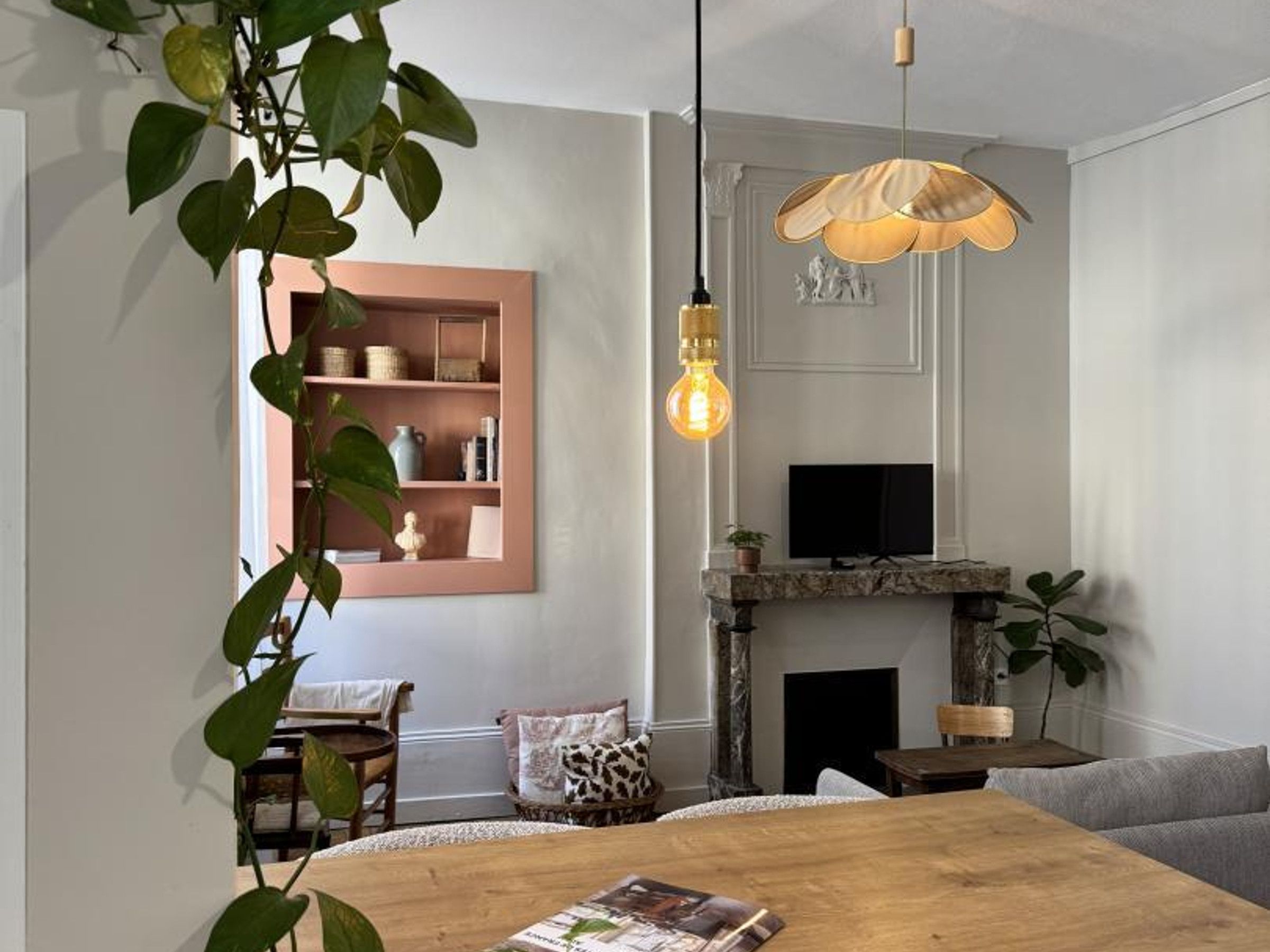 A living room with a fireplace, a television, a wooden dining table, and a hanging light fixture.