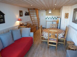 Ein gemütliches Zimmer mit Holzboden, einem roten Sofa, einem Holzesstisch mit Stühlen und einer Küchenzeile im Hintergrund.
