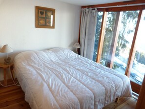 A bedroom with a large bed, a bedside table with a lamp, a window with curtains, and a framed picture on the wall. - Pleasant duplex, valley view - 5 guests (Les Arcs 1800)