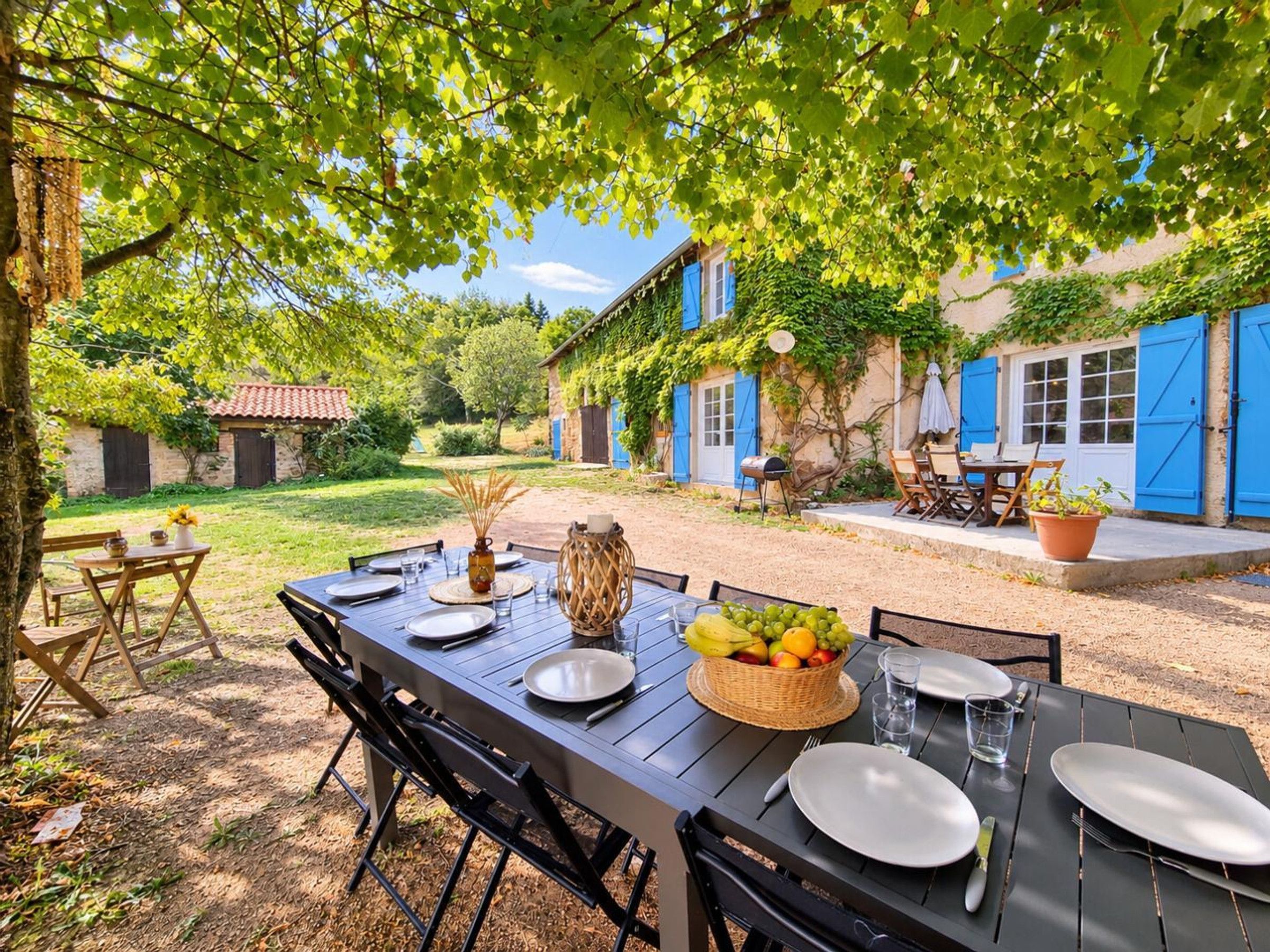 An outdoor dining area with a table set for four, surrounded by trees and a rustic building in the background.