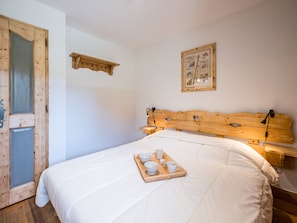A bedroom with a wooden headboard, a bedside table, a tray with cups and bowls, and a framed picture on the wall. - Spacious apartment with terrace and pool (Les Menuires)