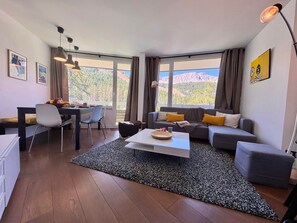 A modern living room with a dining area, large windows, and a view of mountains. - Cozy apartment - 5 guests (Vars)